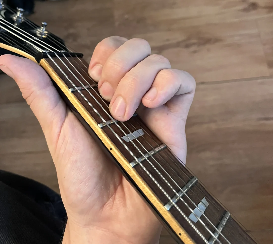A left hand holding a Am chord on a guitar neck, seen from the player's viewpoint with the nut visible for reference