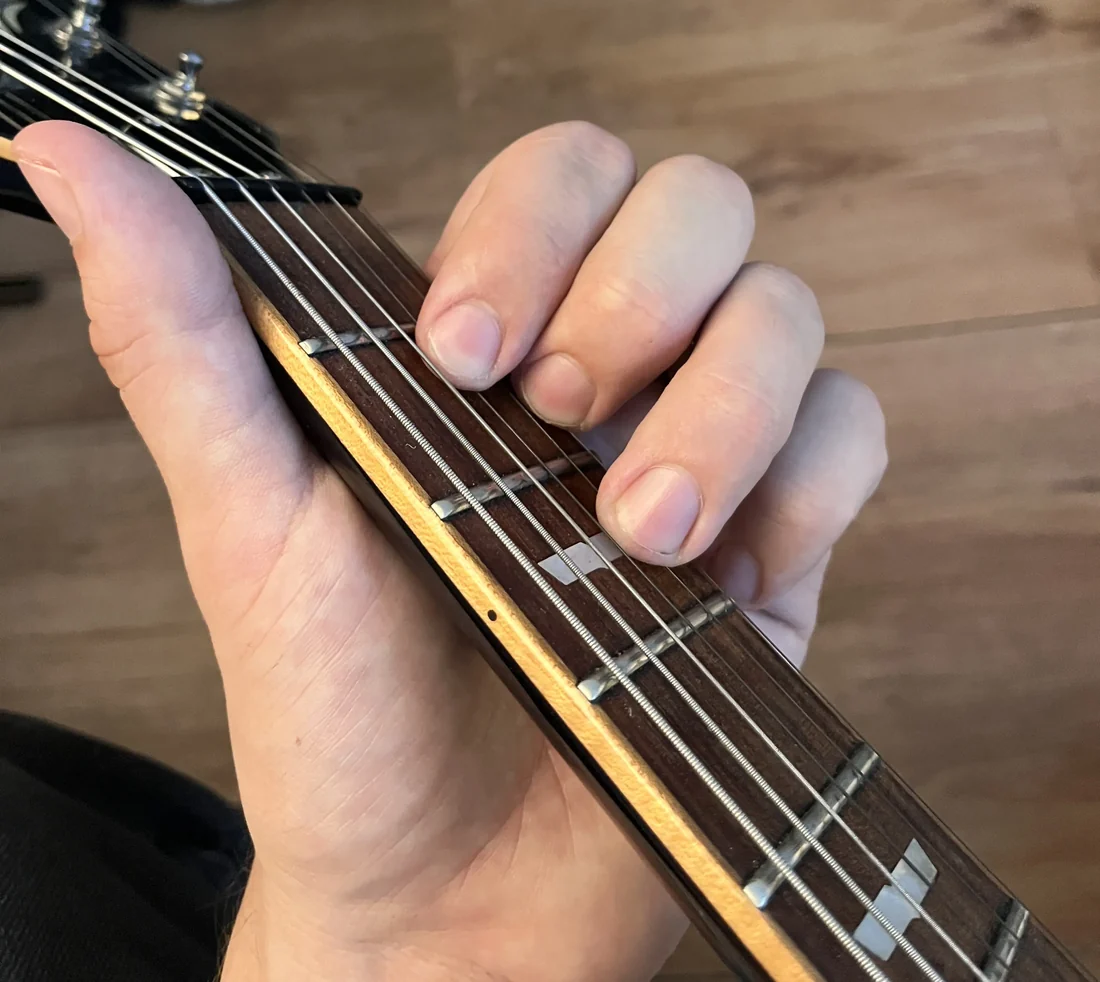 A left hand holding a D chord on a guitar neck, seen from the player's viewpoint