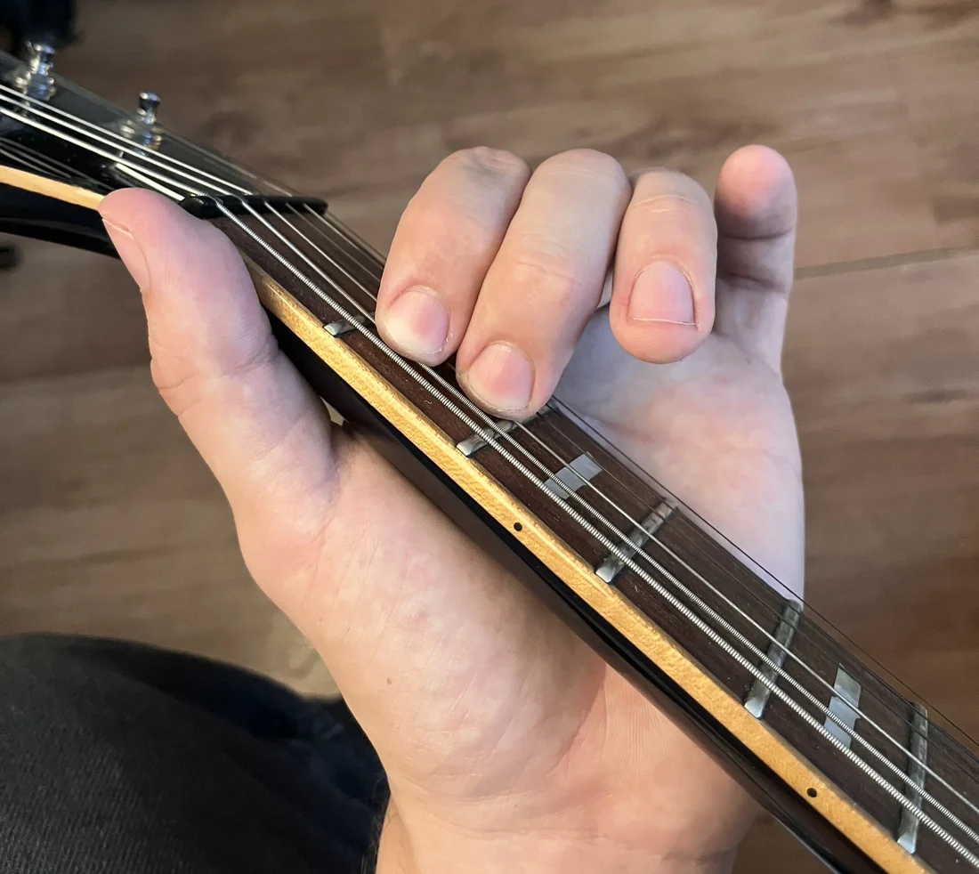 A left hand holding a Em chord on a guitar neck, seen from the player's viewpoint with the nut visible for reference