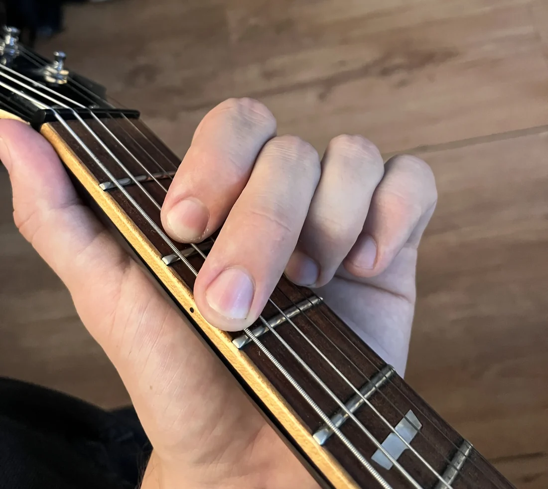 A left hand holding a G chord on a guitar neck, seen from the player's viewpoint